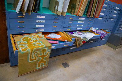 A small tapestry rests on an open drawer of a cabinet for storing many flat objects.