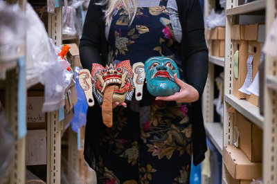 A curator holds two fanciful masks.