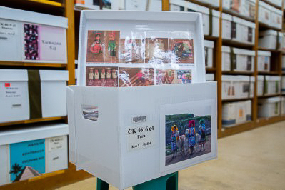 An open box with art objects sits on a row of shelves filled with neatly labelled boxes.