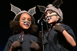 Two children dressed up as bats talking into a microphone.