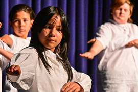 Children in white shirts dancing on stage.