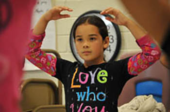 A student holds a pose with arms arching over her head.